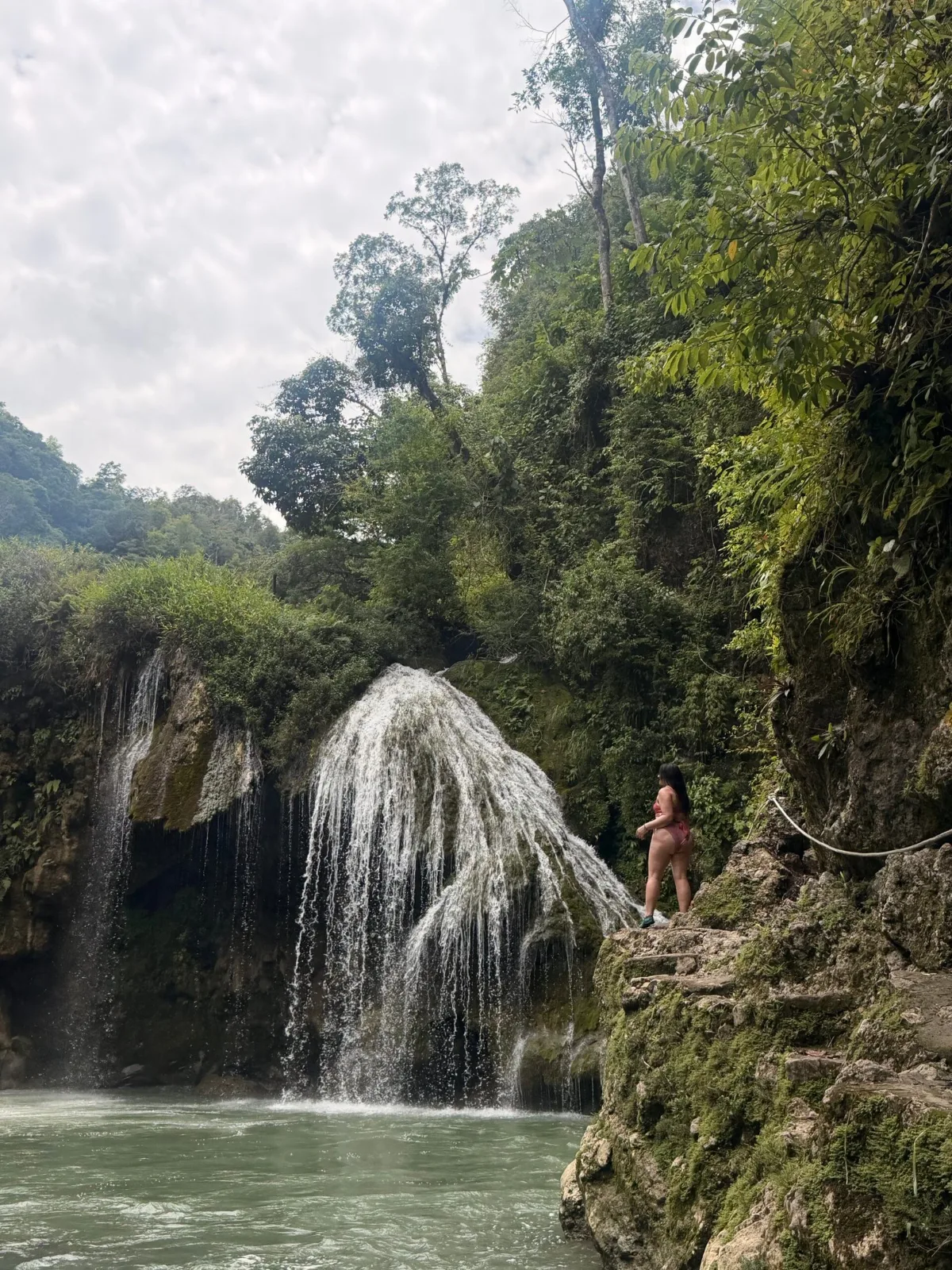Cascada rodeada de selva en Semuc Champey, Alta Verapaz, Guatemala, con una viajera sobre las rocas