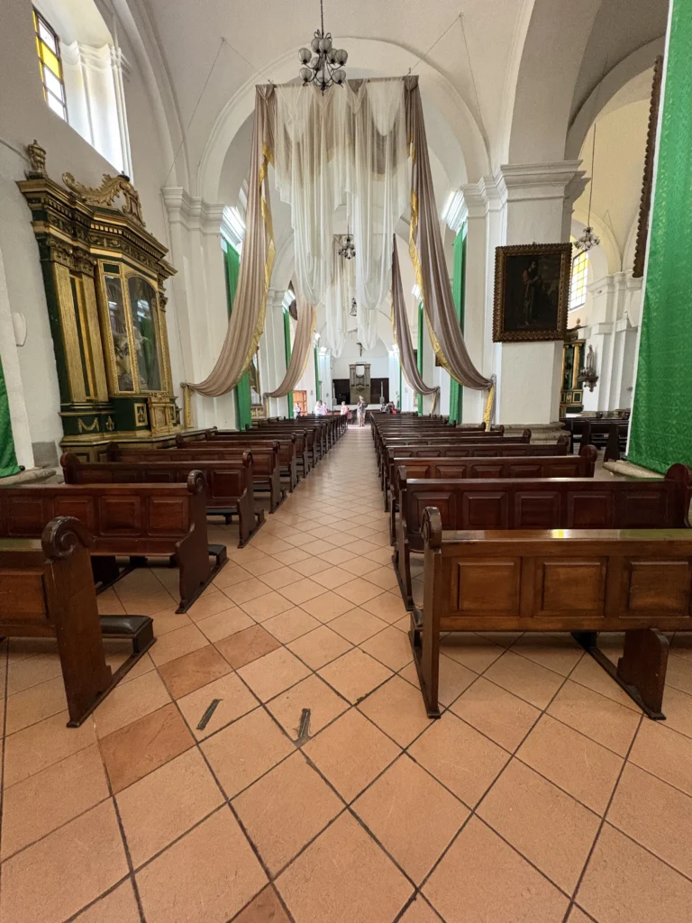 Nave central con bancas de madera y cortinajes en la Catedral de Antigua Guatemala