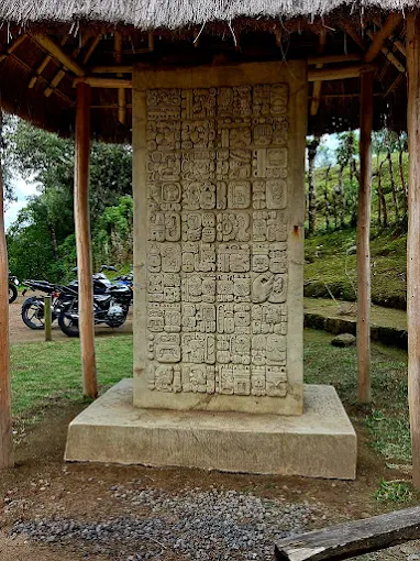 Monumento de piedra tallado con glifos mayas bajo techo de palma, Iximché